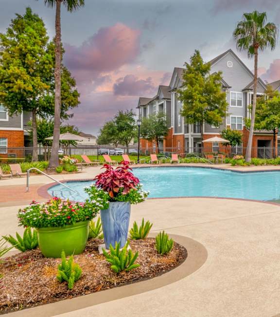 Large swimming pool with red lounge chairs and umbrellas at The Fenwick Apartment Homes, Humble