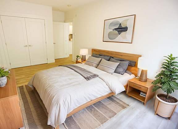 A bedroom with a large bed, a wooden nightstand, and a plant.