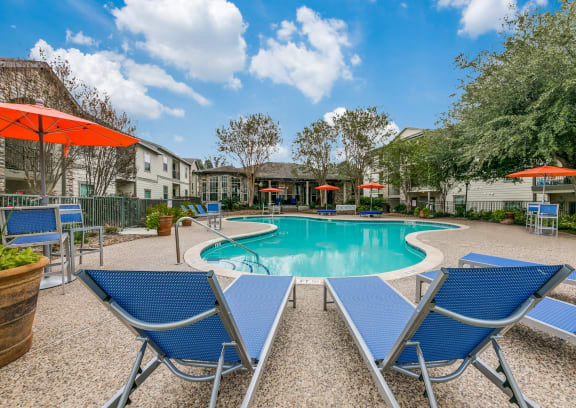 a swimming pool with blue chairs and umbrellas and apartments in the background at Sunrise Canyon, Universal City, TX, 78148