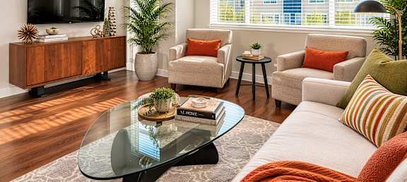A living room with a glass coffee table and a flat screen TV on the wall.