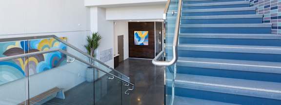 A staircase with a glass railing and a blue tiled wall.