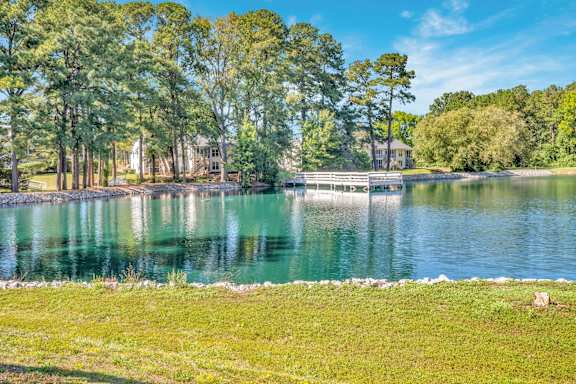 A serene lake surrounded by lush greenery and a wooden dock.