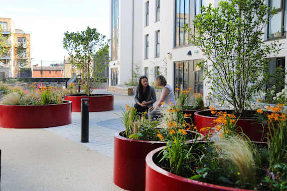 two women looking at plants in a garden outside a building