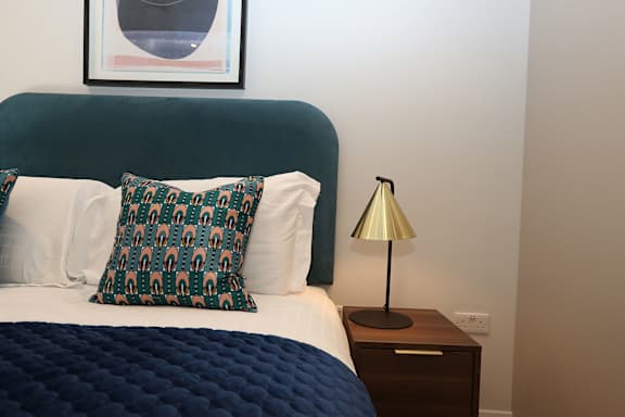 a bedroom with a bed with a blue blanket and a nightstand with a lamp