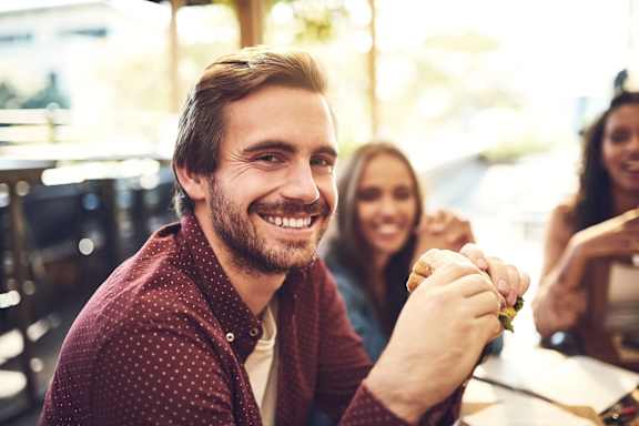 A man is smiling while holding a sandwich in a restaurant.