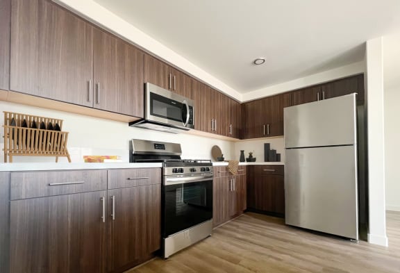 a kitchen with stainless steel appliances and wooden cabinets at The Max on Jefferson Apartments, California