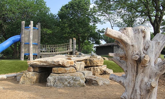 a playground with a tree stump bench and a slide