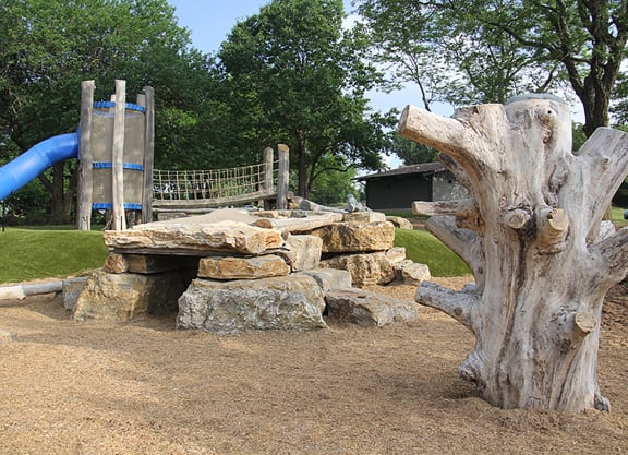 a playground with a tree stump bench and a slide