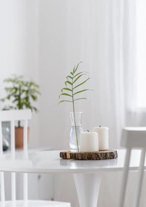 a white dining table with candles and a plant in a glass vase on top