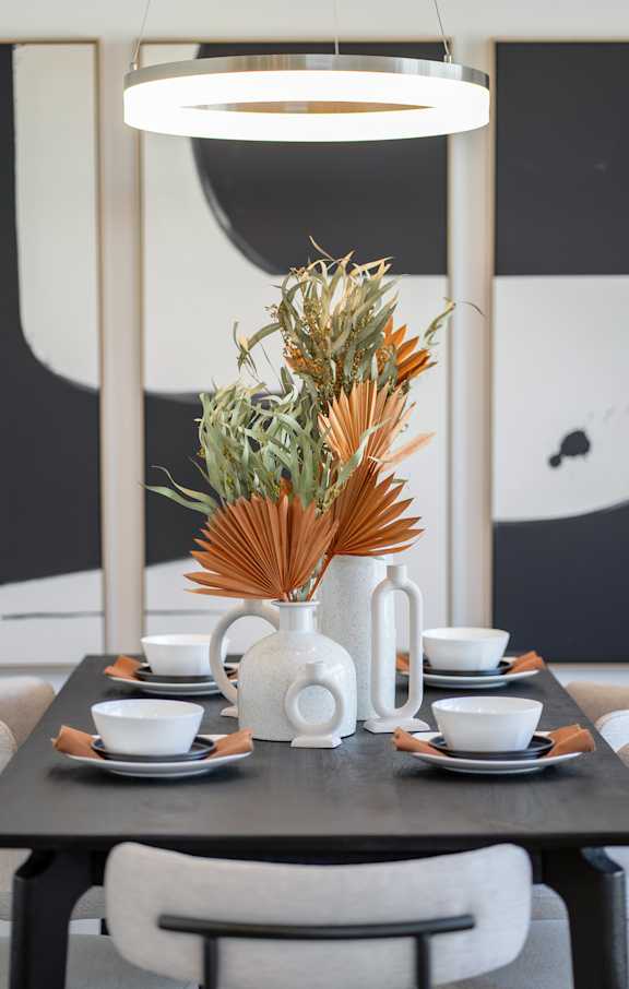 A table set for a meal with a vase of dried flowers as the centerpiece.