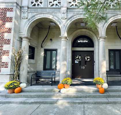 A building with a black door and windows is decorated with pumpkins and plants.