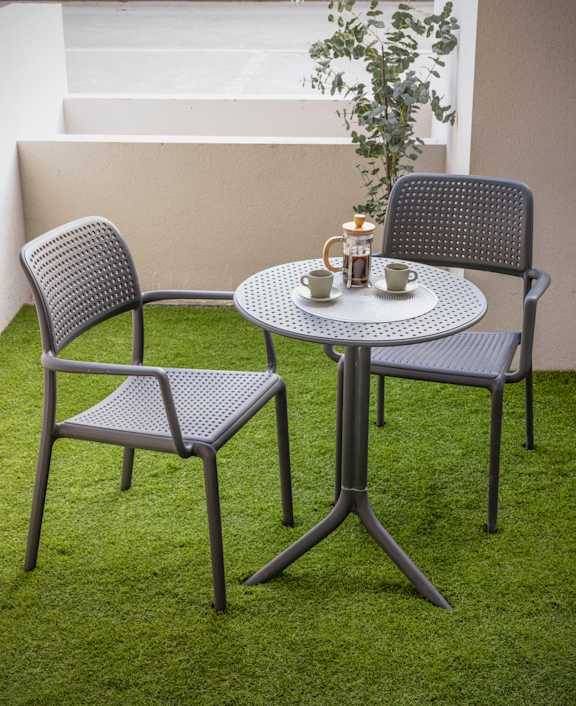 a patio table with two chairs and a coffee cup on it
