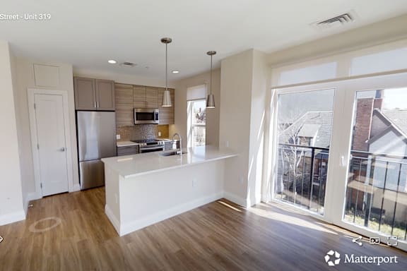 A kitchen with a refrigerator, microwave, and oven is shown in a room with wooden flooring and white walls.