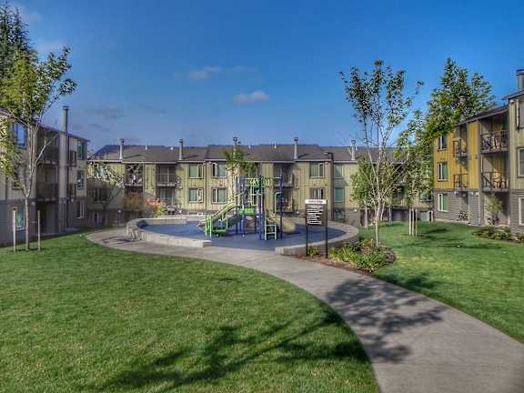 A sunny day at a park with a playground and apartment buildings in the background.