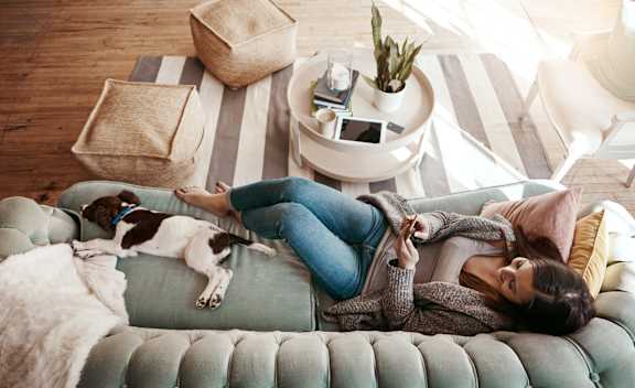 A woman is lying on a couch with her dog at The Woodlands Apartments, Milton Keynes