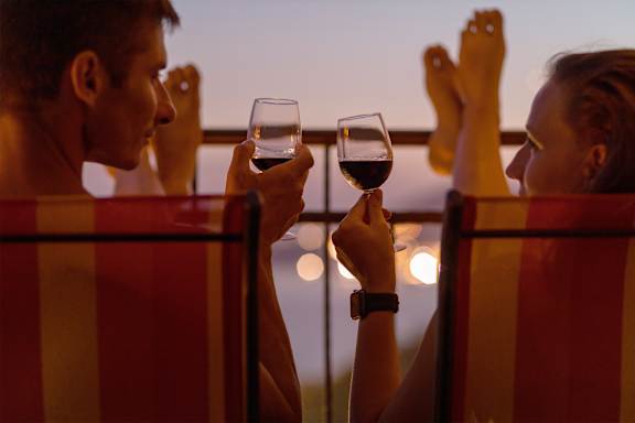 Two people toasting with wine glasses on a balcony.