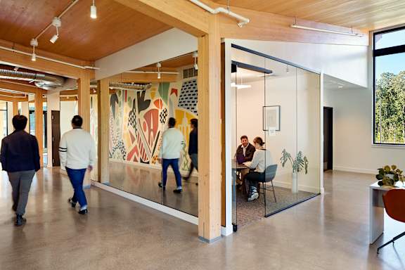 People walking in a hallway with a large painting on the wall.