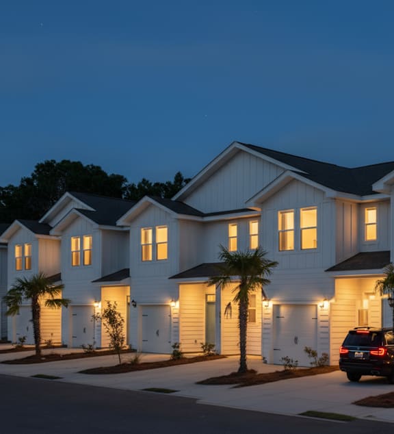 A row of houses with lights on and a car parked in front.