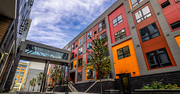 A modern building with orange and grey exterior and a tree in front.at Center Square Lofts East, Pennsylvania, 18101