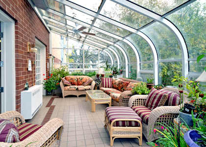 A sunroom with a glass ceiling and walls, furnished with wicker chairs and tables.