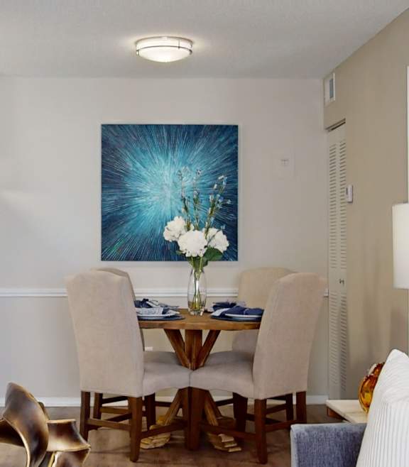 A dining room with a table set for six and a painting on the wall.