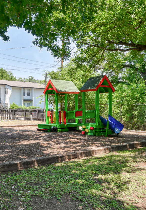 a tree in a park with a playground in the background  at Mayfield Gardens, San Antonio, Texas