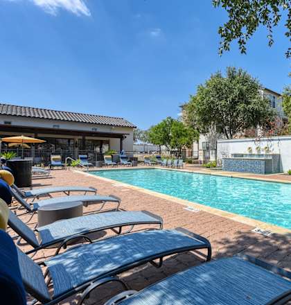 A pool surrounded by lounge chairs and trees.