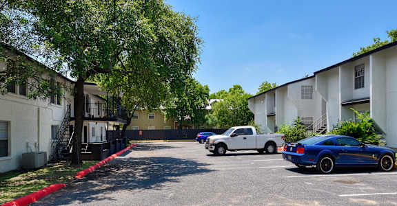 a parking lot between two apartment buildings with cars parked in front