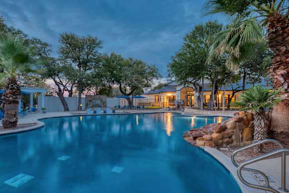 A swimming pool surrounded by palm trees and a building in the background.