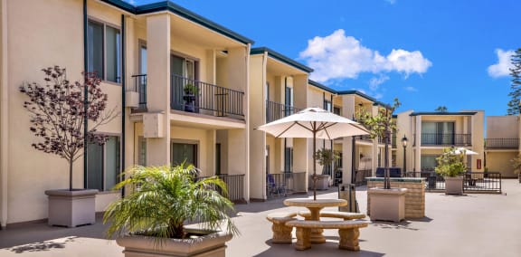 a courtyard with tables and umbrellas in front of apartments at Casa Del Amo Apartments, Torrance, CA 90505
