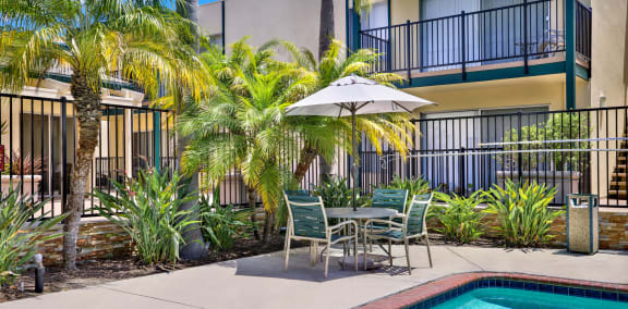 a swimming pool with a table and chairs under an umbrella at Copa Triana Apartments, California, 90505