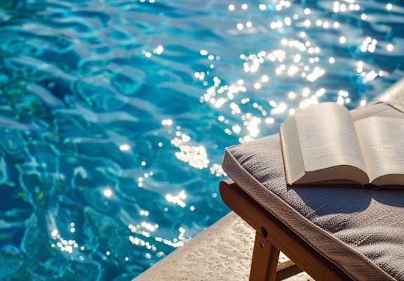 An open book is placed on a lounge chair by the poolside.