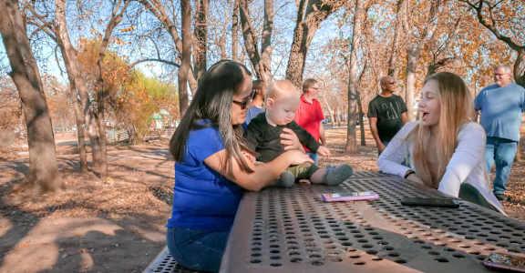 A family is sitting at a picnic table in a park.