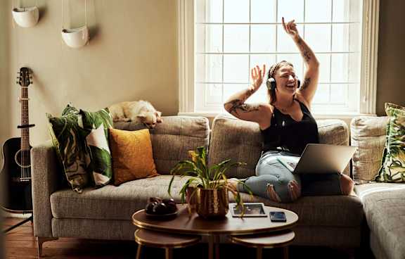 Woman is sitting on a couch with her laptop and headphones on, dancing or celebrating at Alena on Haley, Santa Barbara, CA, 93101