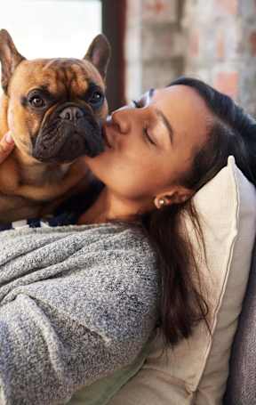 A woman is lying on a grey couch with her dog in her hands at Eastpark Apartment Homes, Salem, OR 97301
