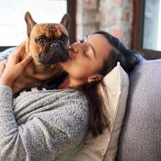 A person laying on a grey couch with a dog in arms at Woodburn Place Apartment Homes, Woodburn, OR, 97071