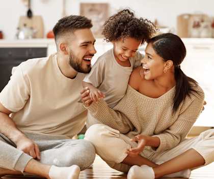 A man and a woman are sitting on the floor with a child, all are smiling and appear to be happy.