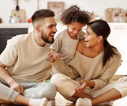 A man and a woman are sitting on the floor with a child between them, all are smiling and appear to be happy.
