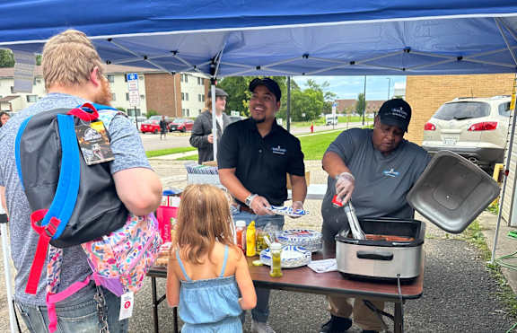 A man and a little girl are standing in front of a table with food on it.