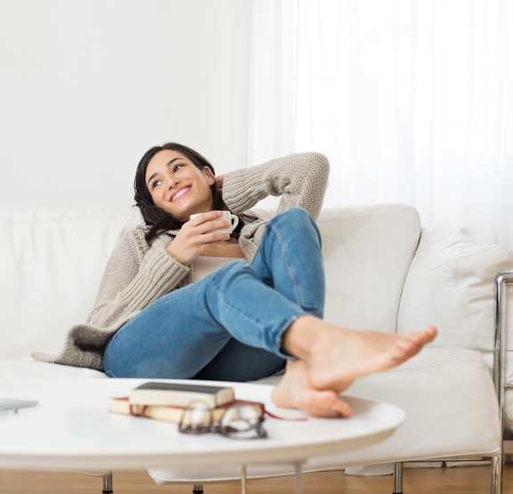 A woman is sitting on a white couch with her feet up on a table.