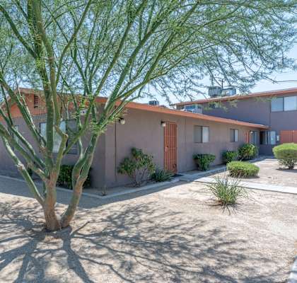 A residential unit with a red roof and a tree in front.