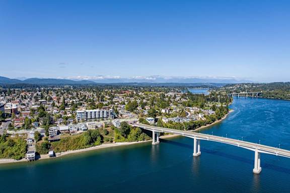 A bridge spans a river in a city with mountains in the distance.