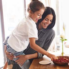 A woman and a young girl are sitting at a table with a bowl of strawberries in front of them.