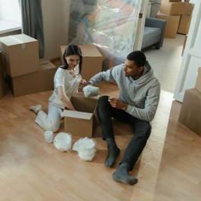 a couple sitting on the floor surrounded by boxes