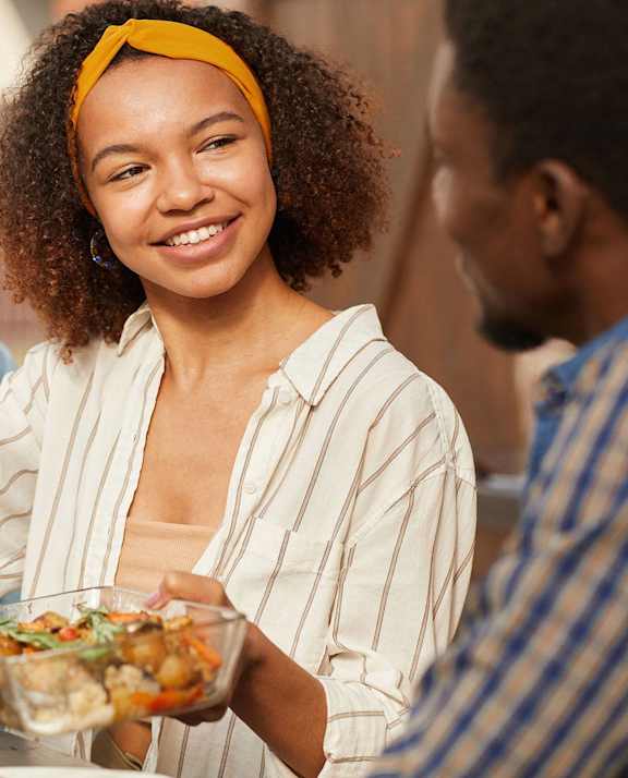 A woman with a yellow headband is serving food to two men at a table.