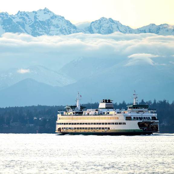 Two ships sailing in the ocean with a mountain range in the background.