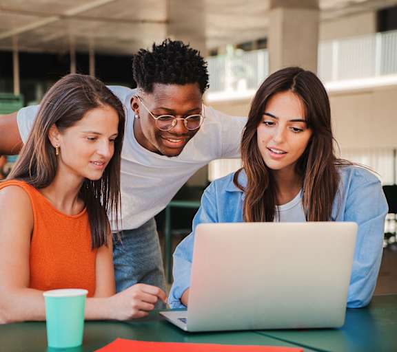 Three people are gathered around a laptop, seemingly engaged in a collaborative activity.