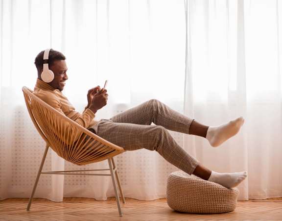 A man is sitting on a chair with his feet up on a cushion, wearing headphones and holding a phone at Stillwater Lakes Apartments, Florida