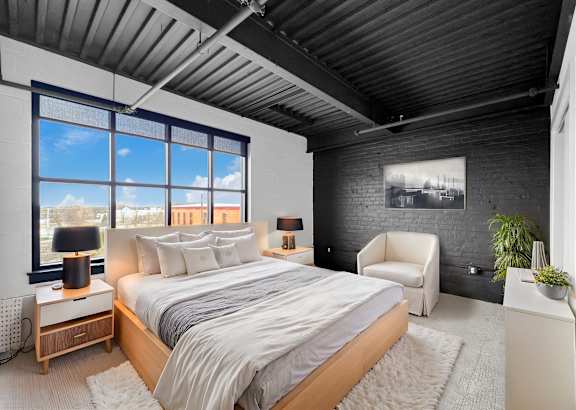 A bedroom with a large bed and a chair.at Plant 1 Lofts, Iowa, 50208