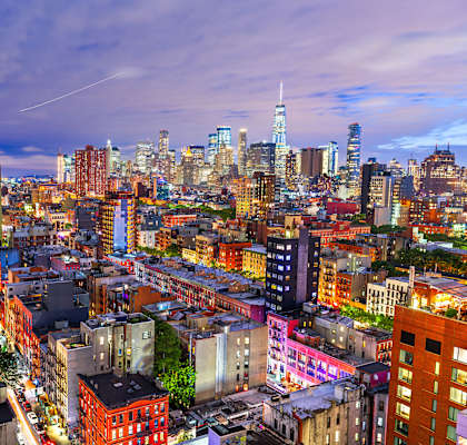 A cityscape at dusk with buildings illuminated and a clear sky.